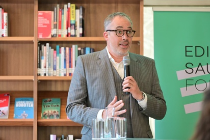 Mann in Nadelstreifenanzug mit Mikrofon in der Hand vor einem Edith Saurer Fonds-Rollup. © ESF / Christopher Glanzl