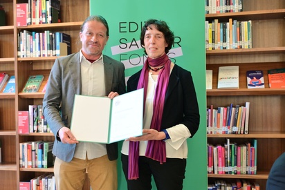 Ein Mann und eine Frau stehen vor einem Bücherregal, sie halten gemeinsam eine Urkundenmappe. © ESF / Christopher Glanzl