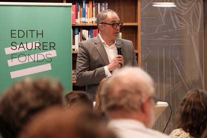 Ein Mann in einem Anzug steht vor einer B&uuml;cherwand und spricht in ein Mikrofon. &copy; ESF / Christopher Glanzl